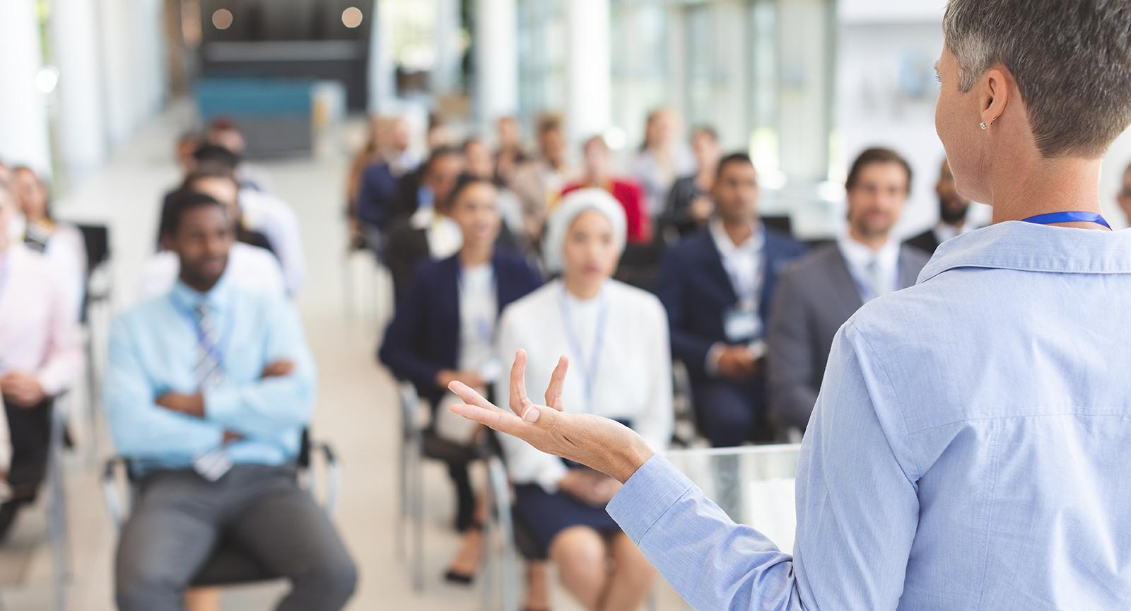 Image of a person standing in front of a sitting audience, sitting