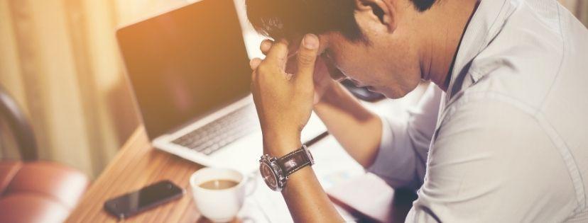 A man leaning over his desk with his hands on his forehead